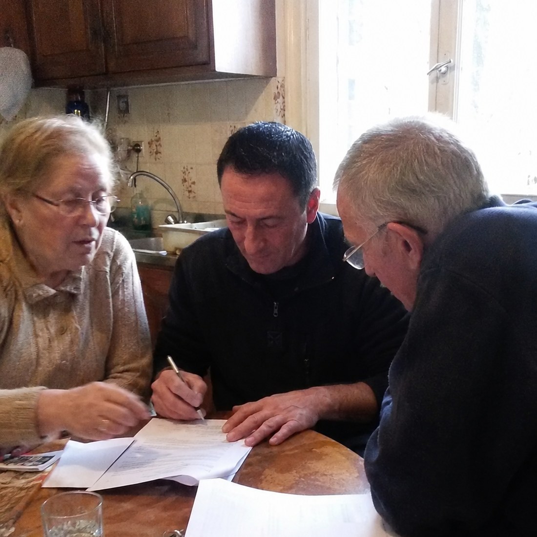 Philippe Arnal fait signer le devis à un couple de clients, à la table de leur cuisine